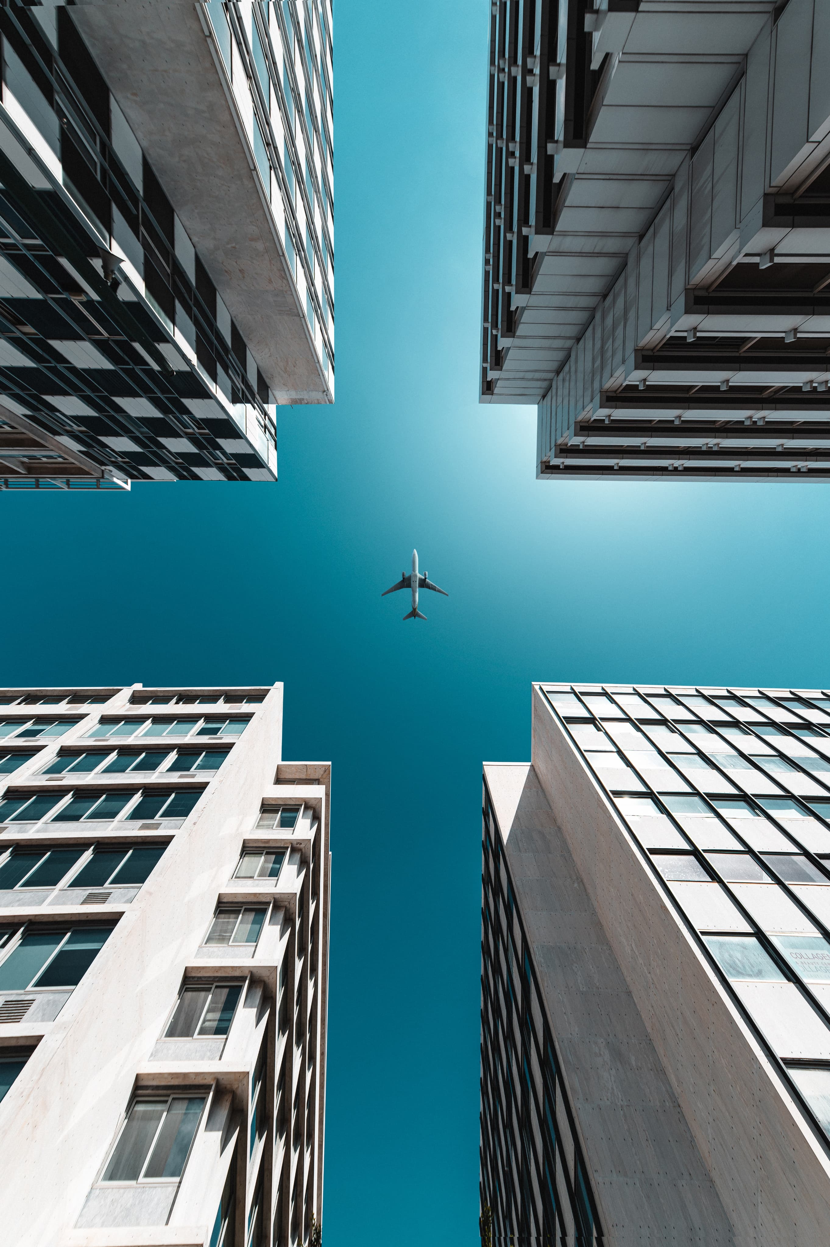 Upward view between modern office buildings and a plane in the sky